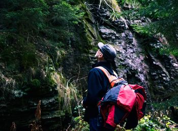 Man looking up while standing by rock formation 