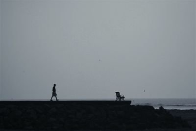 Silhouette woman walking on beach against clear sky