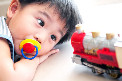 Cute boy sucking pacifier while playing with toy car at home