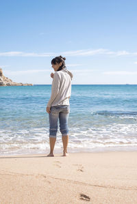 Rear view of a barefoot woman standing on seashore