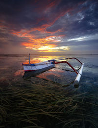 Boat moored on shore against sky during sunset
