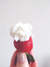 Cropped image of hand holding strawberry against white background