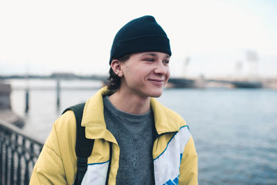 Handsome guy teenager boy 18-19 year old wear knit hat and trendy winter jacket posing at city view