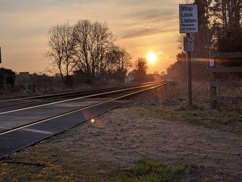 View of railroad tracks by road against sunset sky