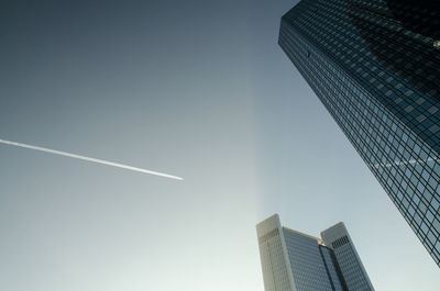 Low angle view of modern buildings against vapor trails in clear sky