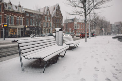 Frozen bench on road against buildings