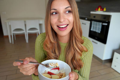 Girl eating muesli granola oatmeal with dried fruits and yogurt looking to the side at home