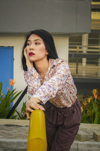 Portrait of young woman looking away while standing against built structure