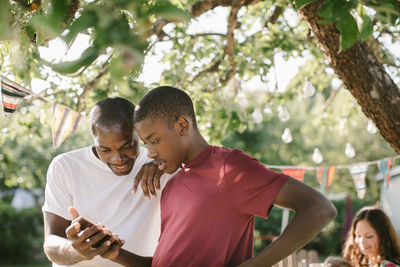 Father and son looking at mobile phone in backyard during garden party