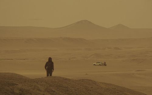 A lonely guy in the desert looks at a car in the distance. full length of man on desert against sky. 