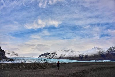 Woman standing on snowcapped mountain against sky