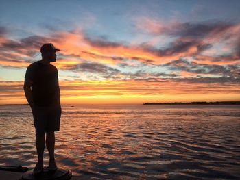 Silhouette man looking at sea against sky during sunset