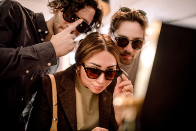 Smiling friends trying fashionable eyeglasses at store