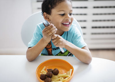 Happy boy looking away while having food at table