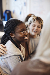 Smiling teenage girl wearing eyeglasses sitting by female friends in group therapy