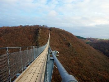 Footbridge hanging on mountain against sky