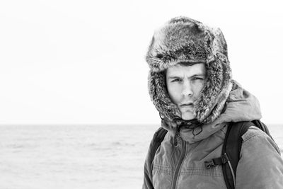 Portrait of man wearing hooded shirt standing against sea