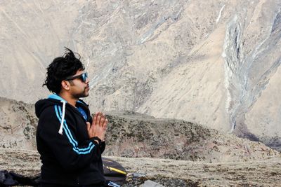 Side view of young man on rock against mountain