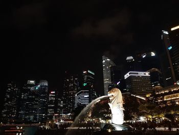 Illuminated modern buildings in city against sky at night