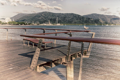 Empty chairs and table on pier by sea against sky