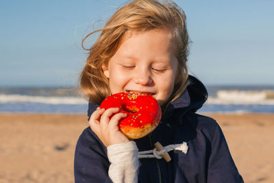 Girl in delight eats donut with red icing, food stained her mouth