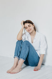 Full length of a young woman sitting against wall