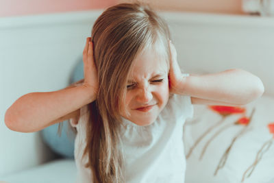 Close-up of girl covering ears on bed at home