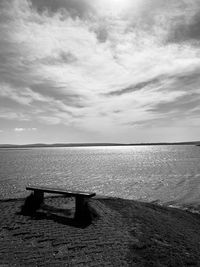 Empty bench on sea shore against sky