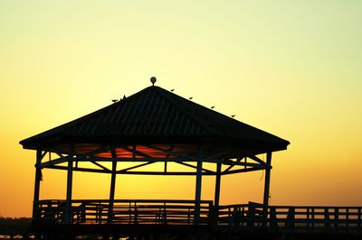 Silhouette bird perching on sea against clear sky during sunset