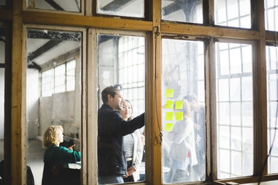 Male it professional discussing plan with businesswoman over adhesive notes seen through glass in office