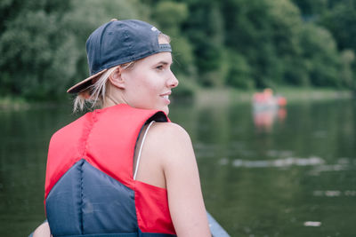 Rear view of smiling young woman wearing life jacket against lake