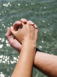 Cropped image of couple holding hands against sea