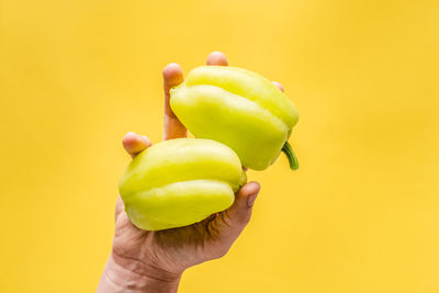 Close-up of hand holding apple against yellow background