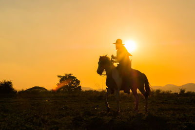View of horse riding on field against sunset sky