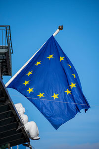 Low angle view of flag against building against clear blue sky