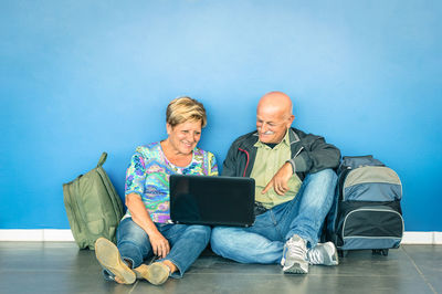 Senior couple using laptop while sitting against blue wall