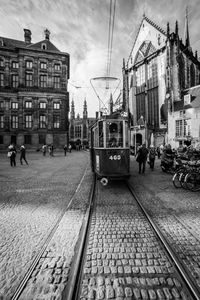 People on railroad tracks in city against sky