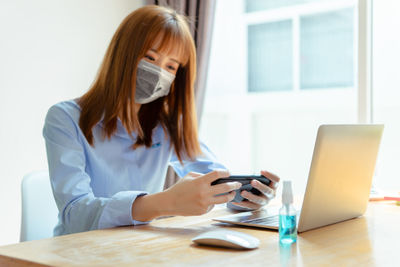 Young woman using phone while sitting on table