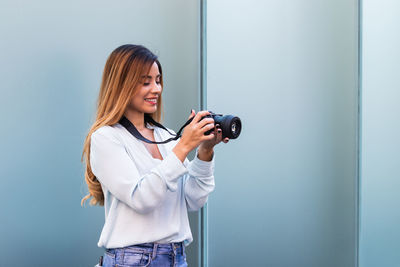 Young woman photographing while standing against wall