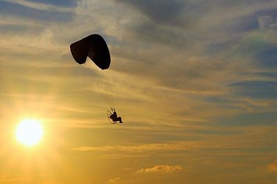 Low angle view of people paragliding against sky during sunset