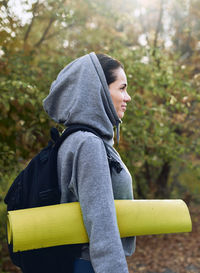 A brunette girl in a hoodie came outside to do fitness with a mat and dumbbells.