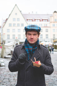 Portrait of a young handsome man in winter clothing holding a dessert