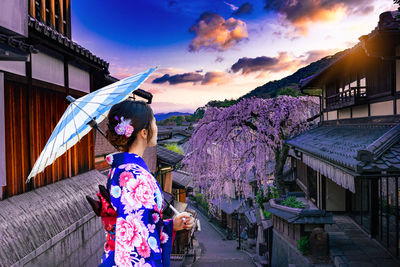 Woman in kimono standing in city during sunset