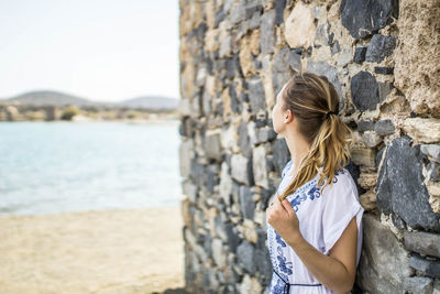 Woman standing by stone wall with sea in background