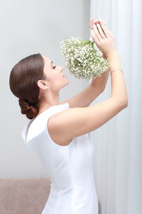 Side view of  woman with uptied hairstyle in wedding dress with arms raised holding bouquet