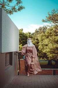 Full length image of veiled woman with white niqab and pink silky dress walking up the stairs