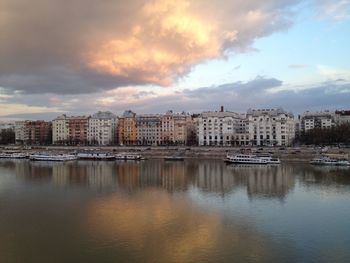 Boats moored at lake against city during sunset