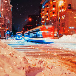 Illuminated street by buildings in city during winter