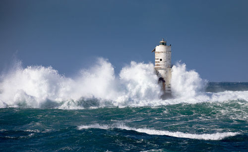 Waves splashing on shore against clear sky