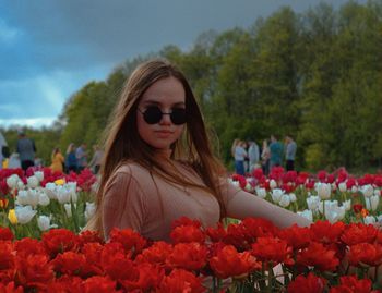 Woman wearing sunglasses against red flowering plants